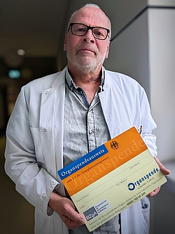 Foto von Oberarzt Siems dem Transplantationsbeauftragten der Universitätsmedizin Rostock auf dem Flur der UMR mit einem großen Organspendeausweis in den Händen.